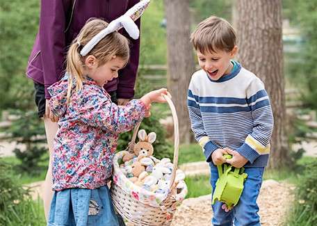 Girl and boy smiling at stuffed toy bunnies in a basket